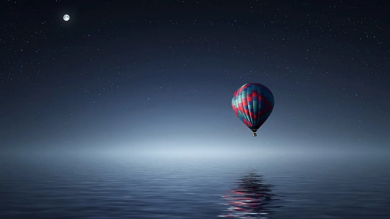 A lone hot air balloon hanging still over calm water under a night sky.