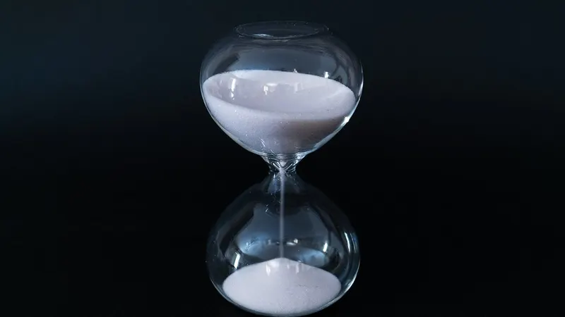 A glass hourglass on a black background with sand trickling through: a schedule counting down to a run that may never fire.