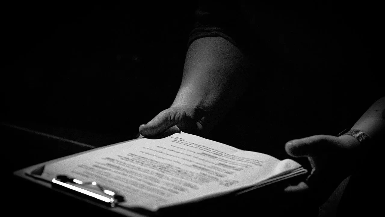 A hand holding a clipboard and document in dim light — the pre-launch review nobody is handed.